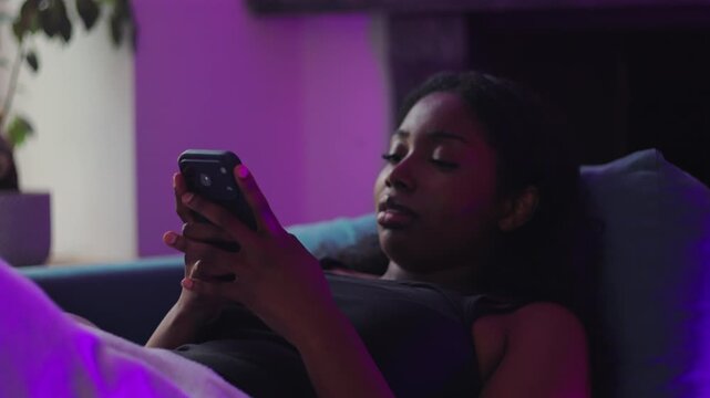 African American woman resting on couch recording voice note on smartphone, expressive speaking moment with relaxed posture, everyday digital interaction in comfortable home setting