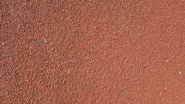 ​A close-up shot of a textured, reddish-brown synthetic running track surface.