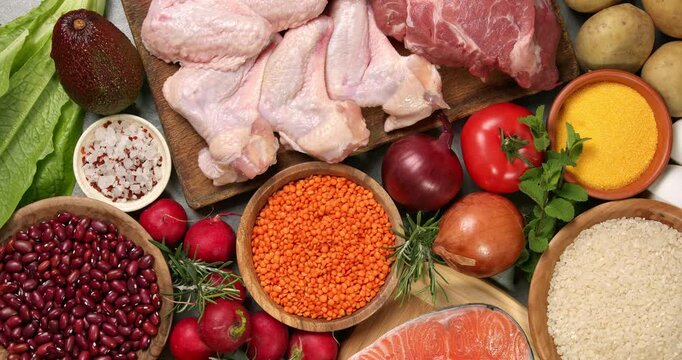 Fresh healthy products on a gray table. Close-up footage of fish, meat, chicken, onion, radish, lettuce, mint, avocado, tomatoes, potatoes, eggs, rice, beans, lentil pasta, corn porridge.