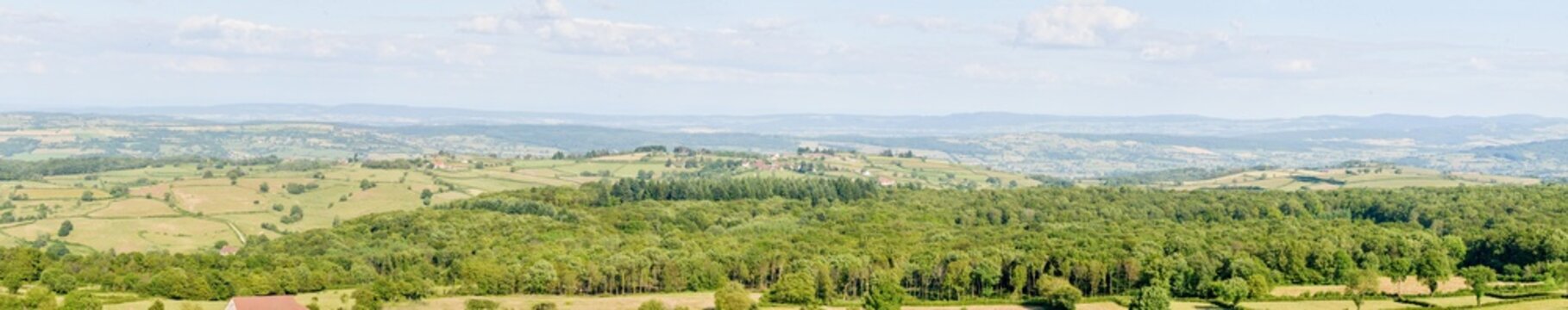 Wide panoramic landscape of rolling hills forests and green meadows in southern Burgundy creating a tranquil countryside atmosphere beneath a bright summer sky