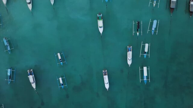 Top down aerial view of traditional wooden outrigger boats and speedboats anchored in turquoise tropical ocean water