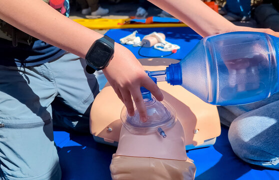 Children learning first aid during cpr training on a medical mannequin. Kids practicing artificial ventilation using an ambu bag resuscitator.