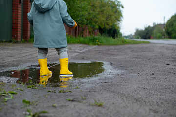 Fototapeta premium Toddler in yellow rain boots splashing in puddle Copy Space