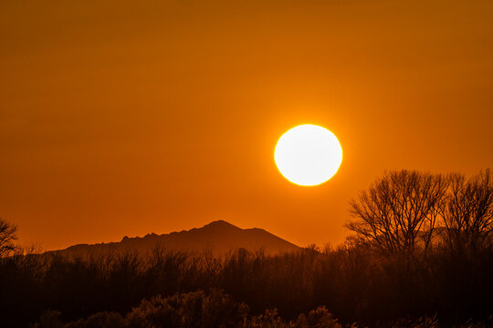 Sun setting above hills against orange sky