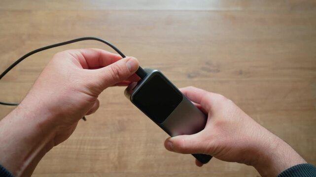 Male hands inserting USB cable into power bank portable charger close up modern external battery device. Connecting mobile charging accessory indoor wooden table minimal tech lifestyle. Preparing