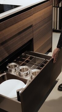 ertical video. Woman closing modern kitchen drawers with organized storage space and cookware. Close-up stylish kitchen furniture and contemporary interior design. Slow motion 4K video.