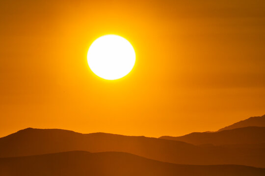 Sun setting above hills against orange sky
