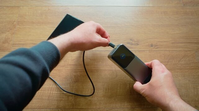 Plugging USB cable into power bank and smartphone close up portable charger powering mobile device. Establishing connection between external battery and phone while charge level indicator visible on