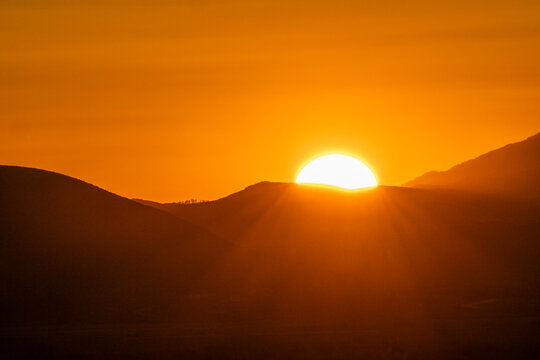 Sun setting above hills against orange sky
