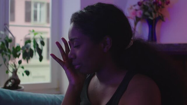 African American woman sitting on couch showing fear and emotional distress, touching face while struggling with inner turmoil, anxiety, and unresolved trauma in quiet home environment