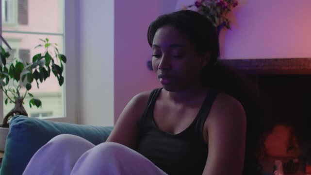 African American woman resting on couch near window with distant gaze expressing quiet sadness emotional overwhelm solitude reflection and inner tension in home setting