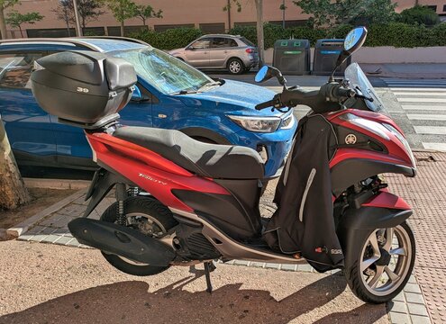 Vista lateral de moto scooter de tres ruedas Yamaha Tricity con ba&uacute;l trasero y manta cubrepiernas estacionada en Madrid, Espa&ntilde;a, 19 de abril de 2026