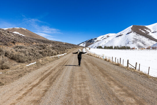 Rear view of woman on empty dirt road in snowy landscape