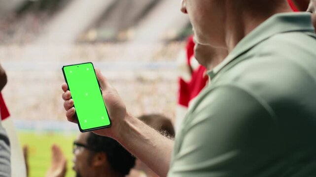 Smartphone chroma key phone held by passionate supporter during live soccer match in a packed football stadium.