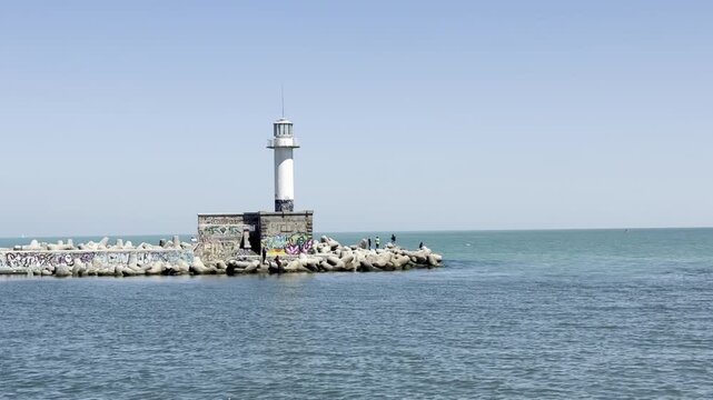 The beautiful clear Black Sea near port Varna, Bulgaria. Lighthouse on rocky pier with graffiti and clear blue sky
