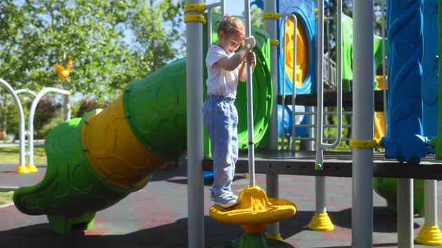 Small girl climbing up yellow steps on a playground structure pole.