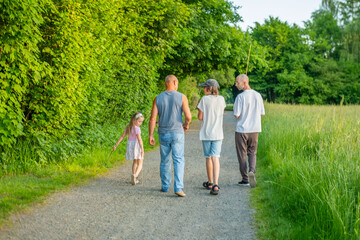 Fototapeta premium multi-generational family grandfathers, teen boy, little girl walking, Loving family fathers children walking together along trail in green European nature park, enjoying outdoor weekend recreation