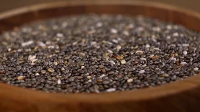 Rotating wooden bowl brimming with raw chia seeds close up showcasing their detailed texture