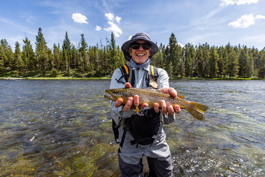 Portrait of smiling fly fisherman holding trout before releasing