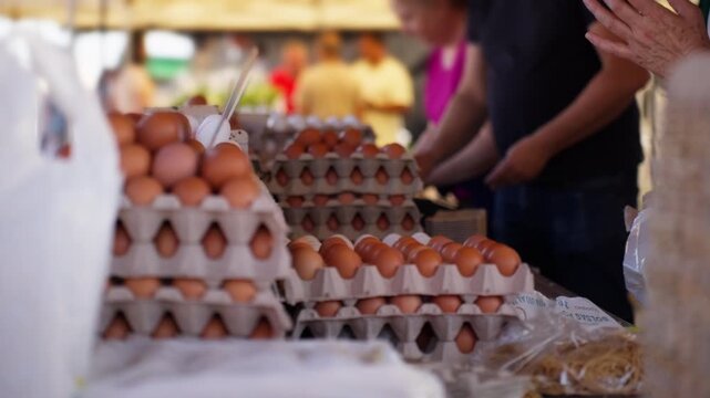 Customers buying fresh organic brown eggs from vendor at busy outdoor farmers market, promoting local agriculture, healthy eating, and sustainable food shopping.