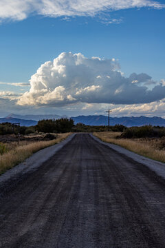 White puffy clouds over empty rural road and mountains