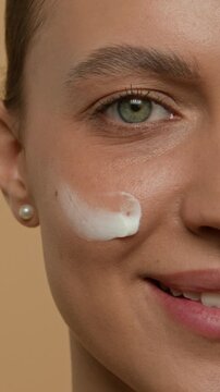 Vertical extreme close-up portrait of young woman gently applying dab of white facial cream to her cheek during beauty routine