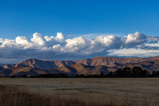 White puffy clouds over mountains and field