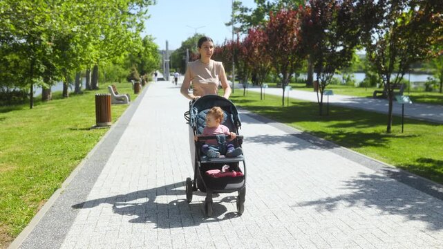 Tracking shot of a mother pushing her small baby in a stroller outdoors.