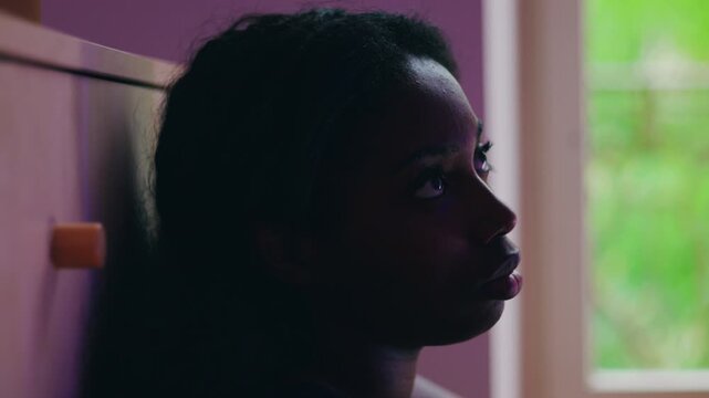 African American woman close up profile by window with distant gaze conveying quiet dissatisfaction introspection and sense of being stuck in unresolved life situation