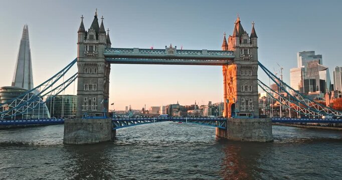 Tower Bridge standing over River Thames with The Shard and other modern skyscrapers in London skyline during a golden hour sunset, showing iconic British architecture at dusk. Aerial view drone flight