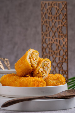 A delicious Indonesian snack called Risol and Risoles filled with chopped vegetables, chicken pieces mayonnaise and fried bread crumbs, served on a white plate on a stone texstured table