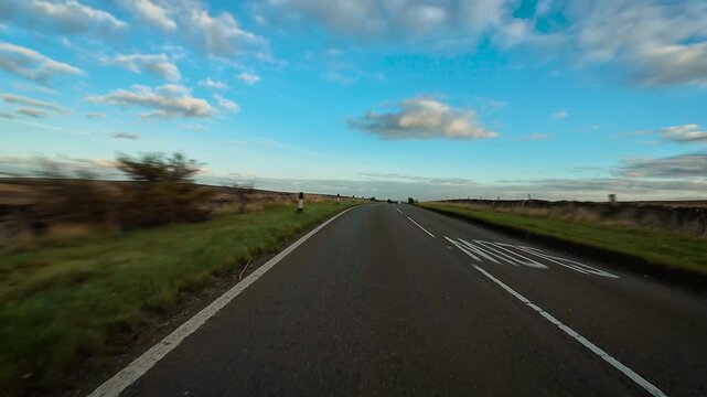 Vehicle driving on winding country road meeting oncoming car under bright sky POV. Automobile moving through rural area surrounded by open fields and soft clouds first person view. SUV traveling along