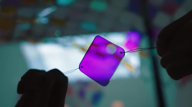 Close-up of hand holding a small glass prism reflecting colorful light