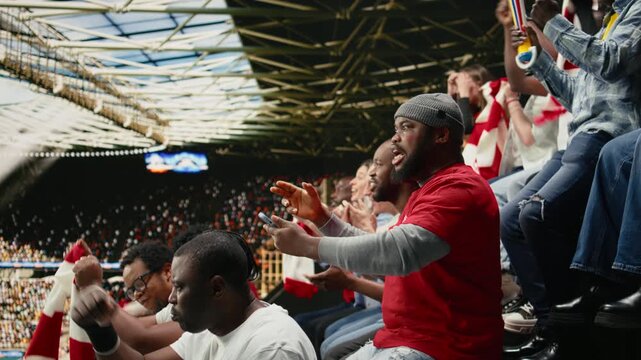 Shocked black fan celebrating betting lucky win with adrenaline, jumping with his friends after final whistle inside the stadium, excited fan reacts to winning ticket mobile bet, jackpot thrill.
