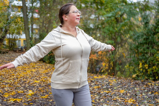plus size woman stretching sideways and swinging arms outdoors on cold autumn morning, doing simple weight loss exercises and fitness, body positivity, healthy sport habits, outdoor exercise