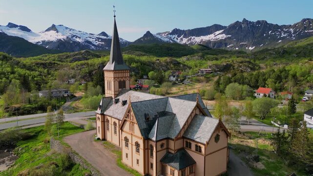 Aerial view of the historic wooden Vagan church in Kabelvag, set against the stunning backdrop of snow capped mountains in the Lofoten Islands