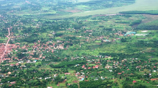 Slowly panning aerial shot capturing the lush green landscape, scattered houses, and rural villages of Uganda, filmed during a flight near Entebbe.