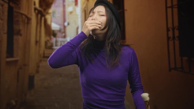 Woman painter covers mouth with hand while holding brush on a narrow cobblestone street, beret tilted, eyes closed; weariness solitude.