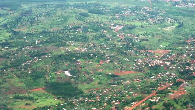 Scenic window-seat view of a passenger plane flying over the lush green landscape, scattered houses, and rural villages of Uganda, filmed during a flight near Entebbe.