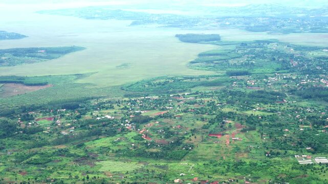 A peaceful window-seat perspective capturing the vibrant green fields, small townships, and winding roads of Uganda during a daytime flight near Entebbe.