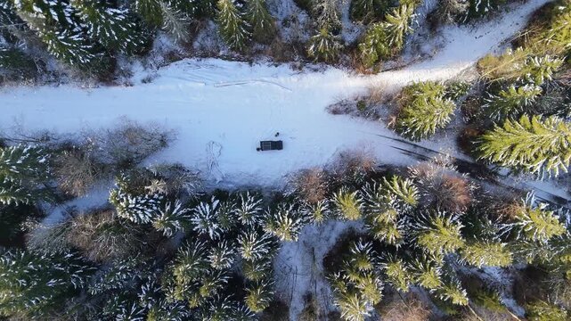 Solar-powered vehicle seen from above as a drone descends over a snowy forest track in Parc naturel r&eacute;gional du Haut-Jura, France, revealing winter pines and tire marks.