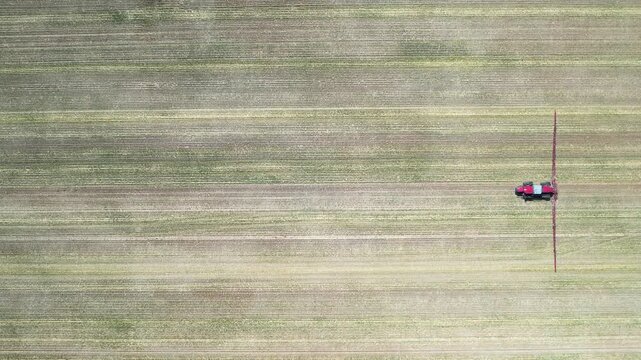 Static top down drone view of tractor boom sprayer moving left to right across patterned crop rows creating strong geometry and illustrating precise large scale agricultural spraying process