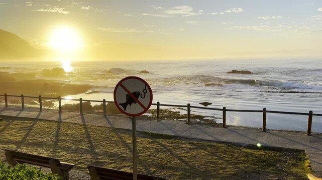 No fishing permitted sign next to marine tide pool in Hermanus at sunrise