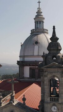 Vertical aerial close-up shot capturing the clock tower, bell towers and dome of the Sanctuary of Our Lady of Sameiro in Braga, Portugal.