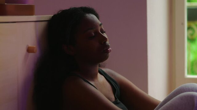 African American woman close up leaning against wall with distant gaze expressing introspection worry and sense of directionless thought during challenging moment indoors