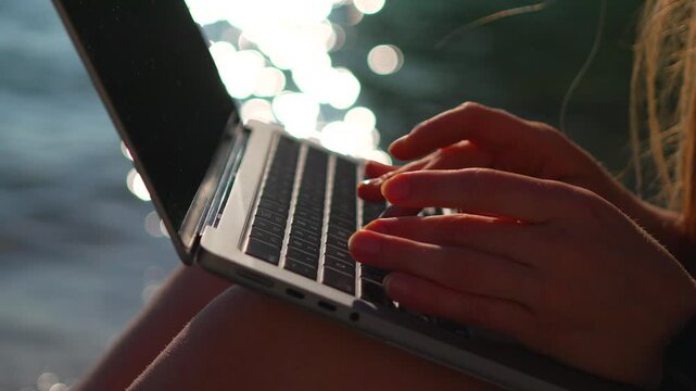 Laptop hands typing while sitting on a beach by the ocean for a remote work or digital nomad lifestyle