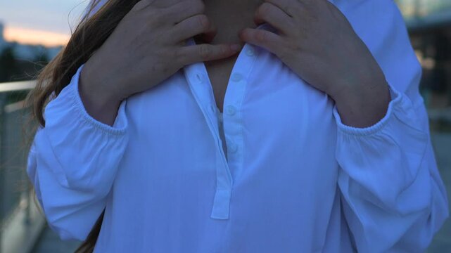 Woman buttoning shirt close up view of a female fastening her white blouse outdoors during a quiet twilight evening