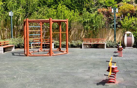 Playground equipment stands in a sunny area with benches and greenery all around