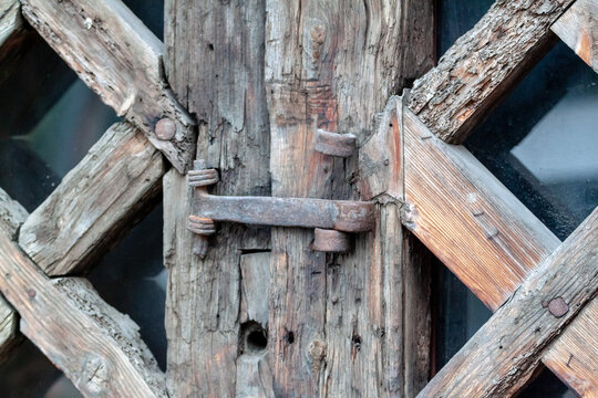 Close up of ancient rusty iron hinge latch on weathered wooden door. Vintage industrial background with rough timber texture and corroded metal hardware details. Cyprus.