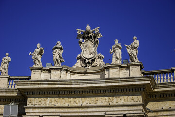 Obraz premium Statues of saints line the colonnade of St. Peter's Square in Vatican City under a clear blue sky.